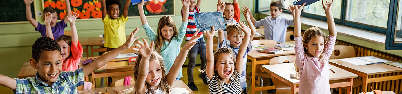 kids in classroom desks with arms lifted