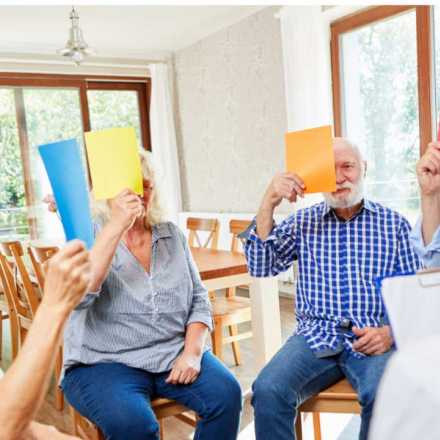 seniors sitting in circle holding colored paper in front of their face