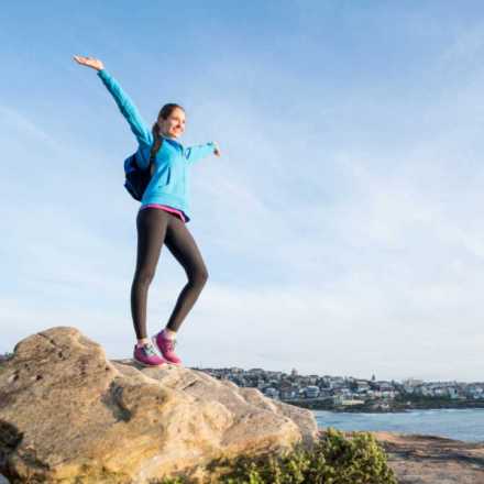 Woman standing on a rock on a beach with her arms in the air smiling