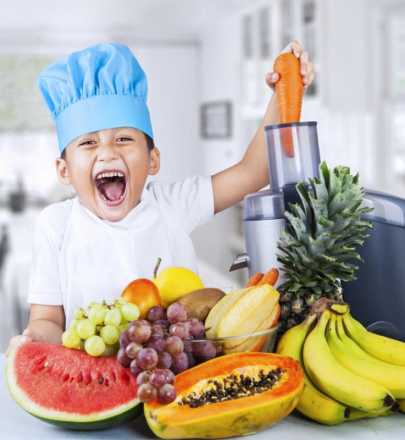 Kid with chef hat on and fruits and veggies in front of him