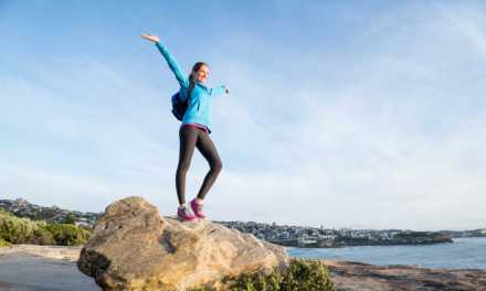 Woman standing on a rock on a beach with her arms in the air smiling