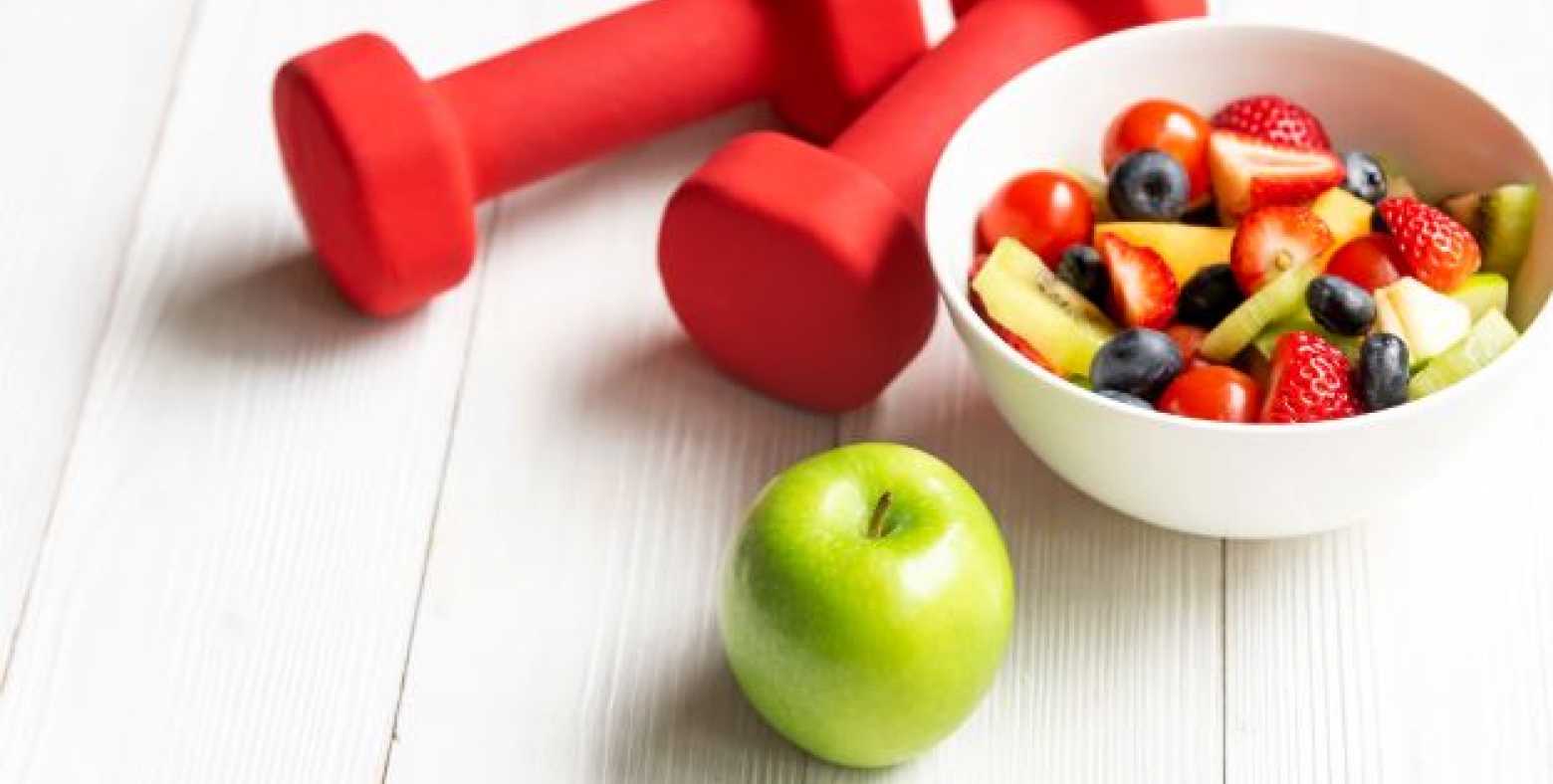 dumbbells, green apple, bowl of cut up fruits