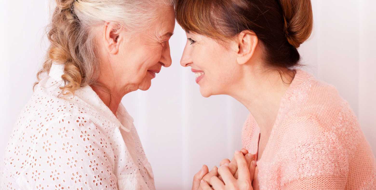 elderly mother and daughter holding hands, smiling face-to-face with foreheads touching